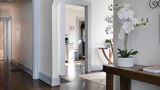 Een modern interieur met een houten vloer, een witte muur met een klok en een orchidee in een pot op een houten tafel.
