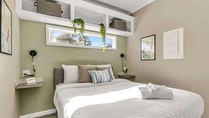 Une chambre bien rangée, avec un grand lit, des tables de chevet, une fenêtre agrémentée de plantes et une vue sur l’extérieur.