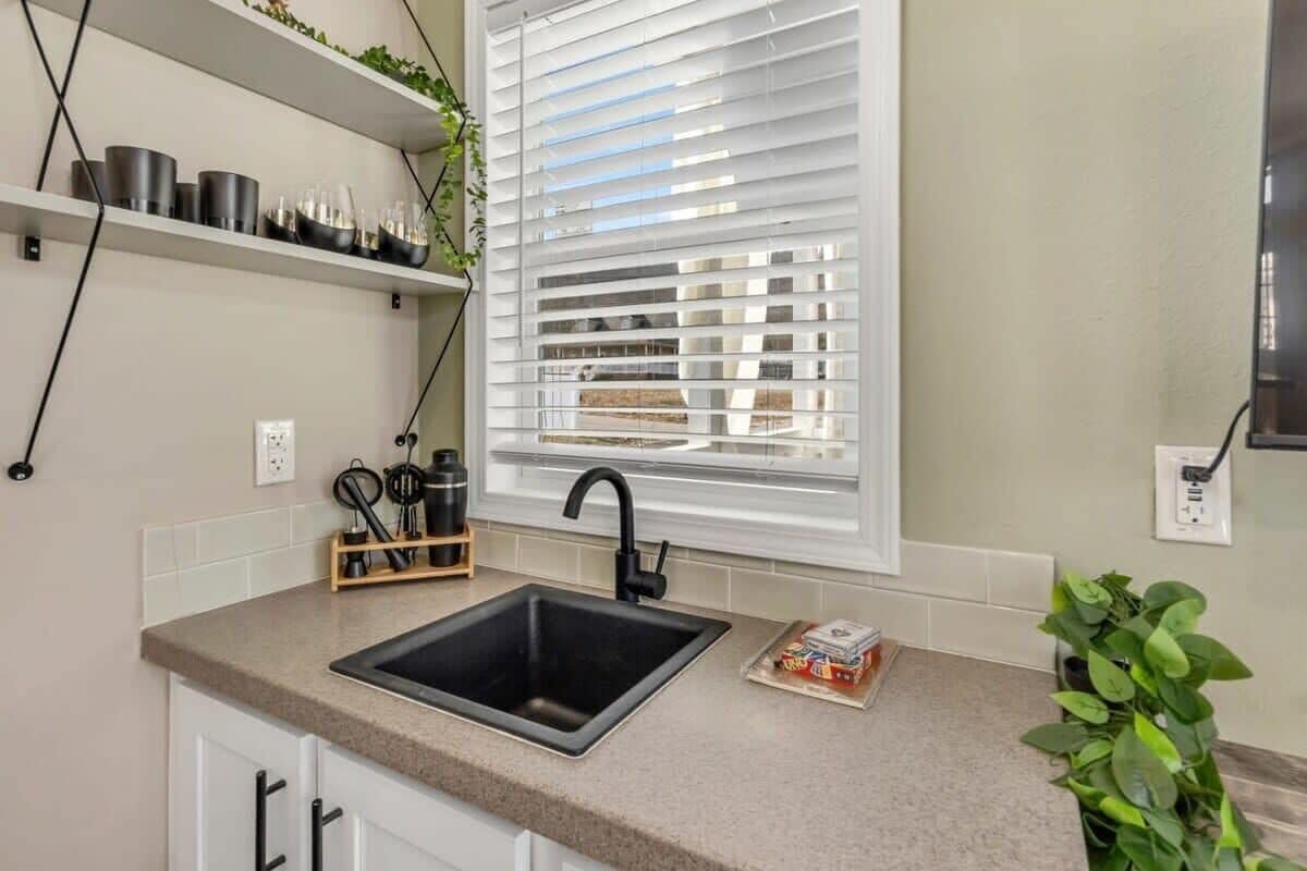 A kitchen with a black sink, white cabinets, a window with blinds, and a plant on the counter.