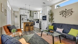 Une cuisine moderne avec des meubles blancs, un îlot central et un coin repas comprenant une table en verre et des chaises orange.