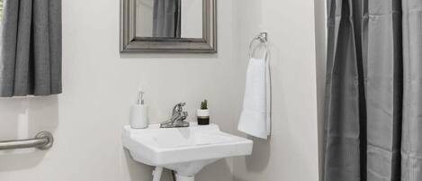 A bathroom with a white sink, a mirror, a towel rack, and a shower curtain.