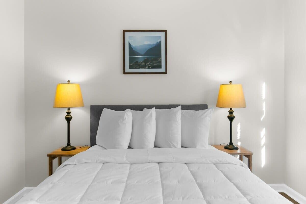 Een net opgemaakt bed met witte beddengoed en twee bedlampen op houten nachtkastjes.