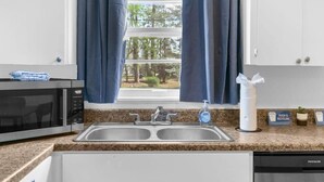 A kitchen with a double sink, a microwave, a dish soap bottle, and a trash and recycling bin.
