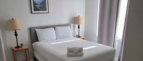 A neatly arranged bedroom with a bed, two bedside lamps, a framed picture on the wall, and a patterned rug.