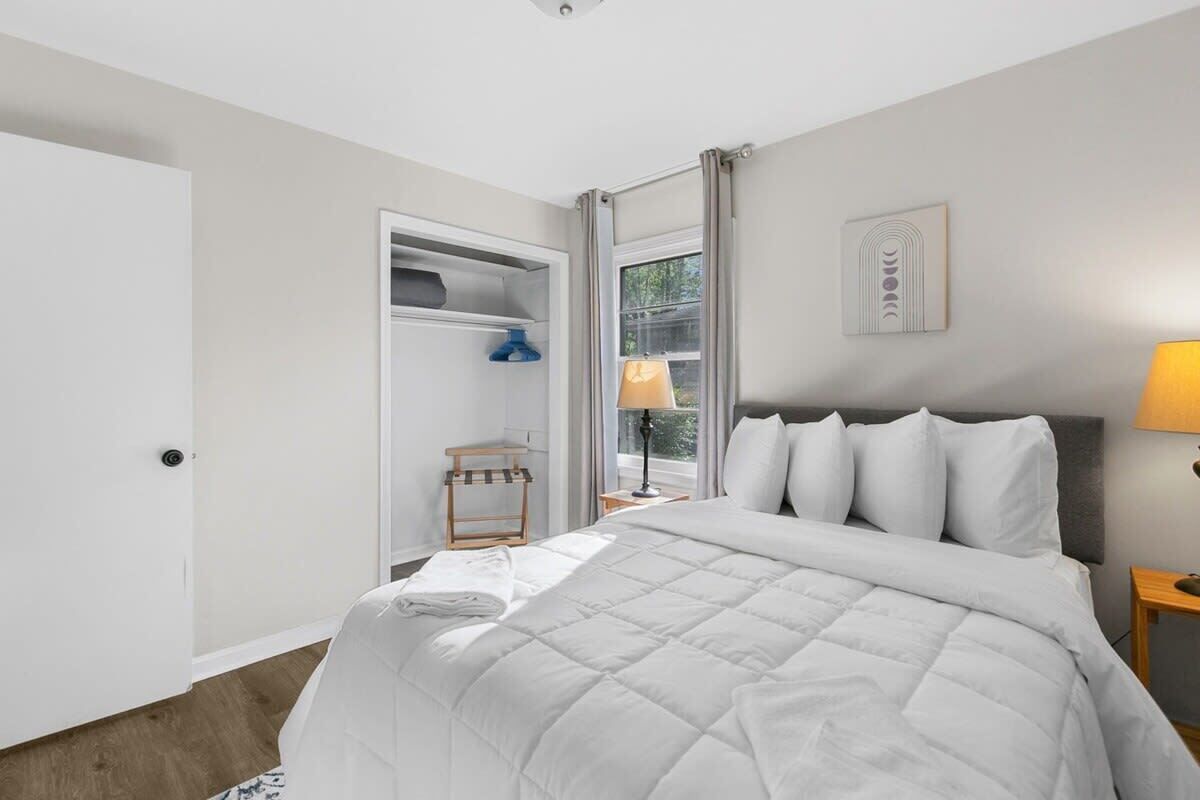 Un dormitorio ordenado con cama, mesita de noche, lámpara y ventana con cortinas.