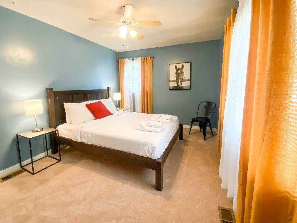Een slaapkamer met een bed, nachtkastje, stoel en plafondventilator.