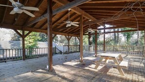 Eine Terrrasse aus Holz mit Picknicktischen und Deckenventilatoren.