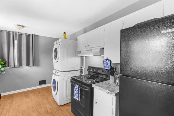 Une cuisine moderne avec un réfrigérateur noir, des armoires blanches, une cuisinière et un lave-linge.