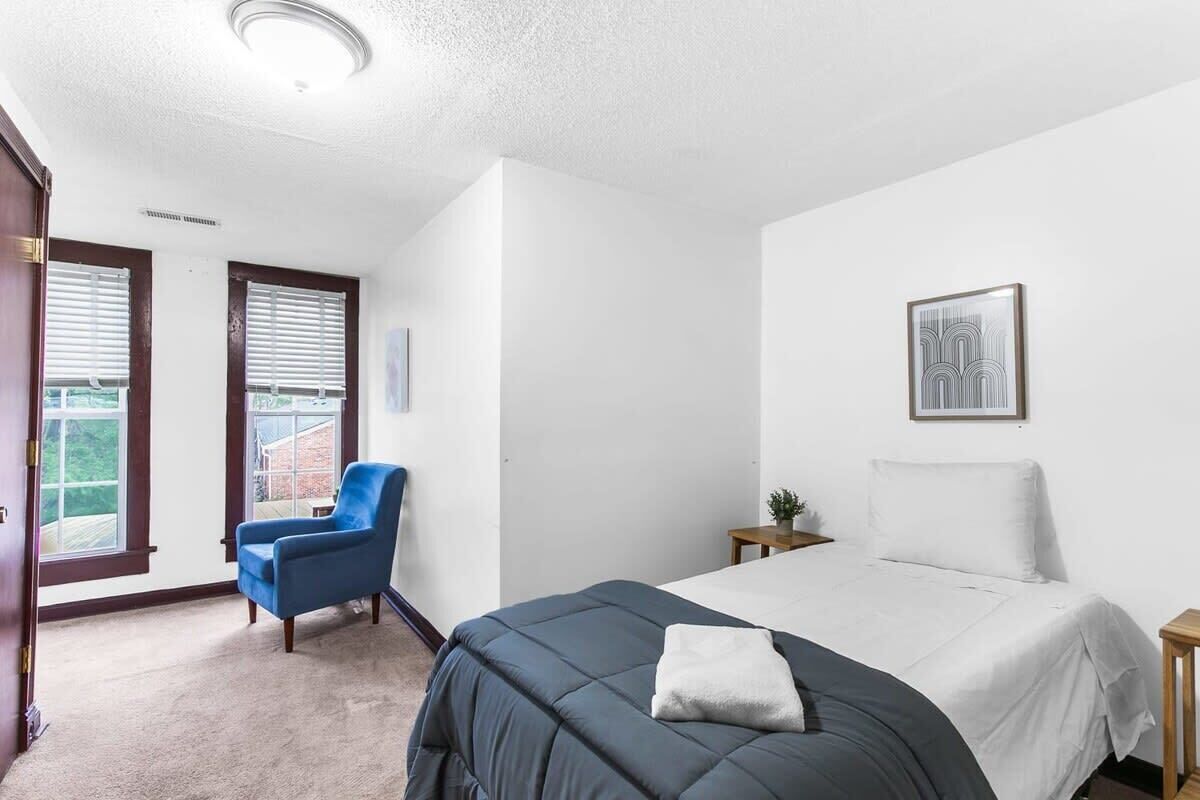 Une chambre à coucher comprenant un lit, une chaise, une petite table, un tableau accroché au mur et une porte donnant sur un balcon.