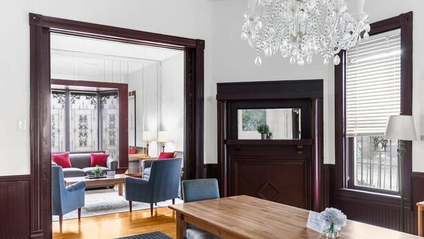 A spacious room with a wooden dining table, blue chairs, a chandelier, and a view of a balcony with a sofa and plants.