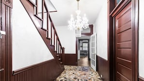A hallway with a wooden staircase, a chandelier, and a tiled floor.