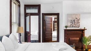 A hotel room with a bed, a lamp, a fireplace, and a painting on the wall.