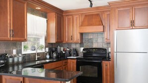 A kitchen with wooden cabinets, a black stove, a stainless steel refrigerator, and a window with a view of greenery. - Highland Drive Hideaway (Birmingham)