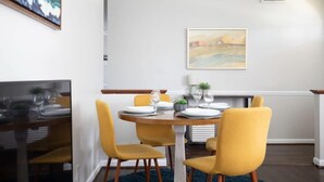 A dining area with a round table set for four, yellow chairs, and a painting on the wall. - Highland Drive Hideaway (Birmingham)