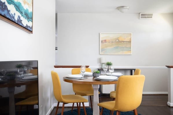 A dining area with a round table set for four, yellow chairs, and a painting on the wall.