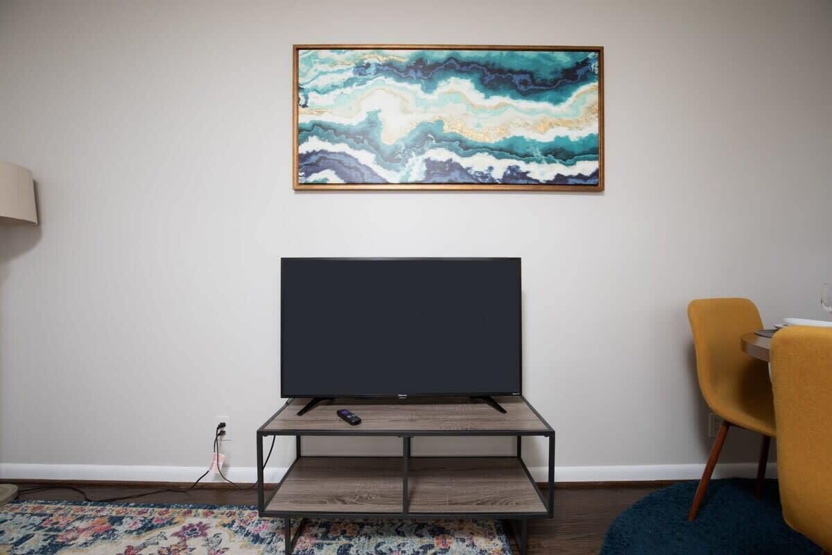 A modern living room with a flat-screen TV on a wooden stand, a colorful abstract painting on the wall, and a yellow chair.