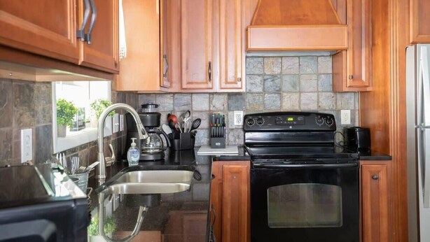A kitchen with wooden cabinets, a black stove, and a stone backsplash. - Highland Drive Hideaway (Birmingham)