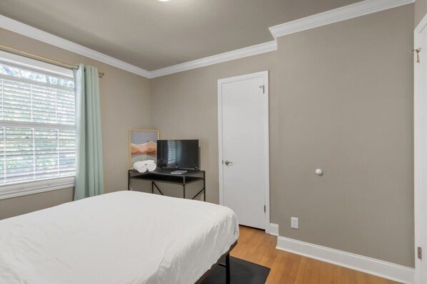 A bedroom with a bed, a television on a stand, a door, and a window with blinds. - Gilmore Retro Pad (Madison)