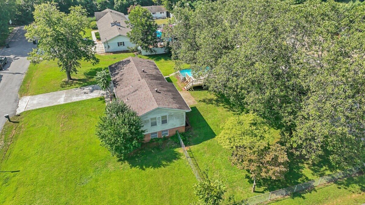 Una casa a un piano con tetto spiovente, circondata da un prato curato e diversi alberi maturi.