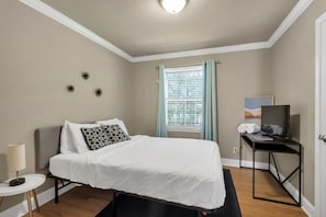 A bedroom with a bed, a desk with a computer, a lamp, and a window with curtains. - Gilmore Retro Pad (Madison)