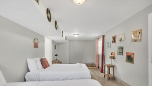 Una camera d'albergo con due letti, pavimento in legno e parete decorata con diverse immagini incorniciate.