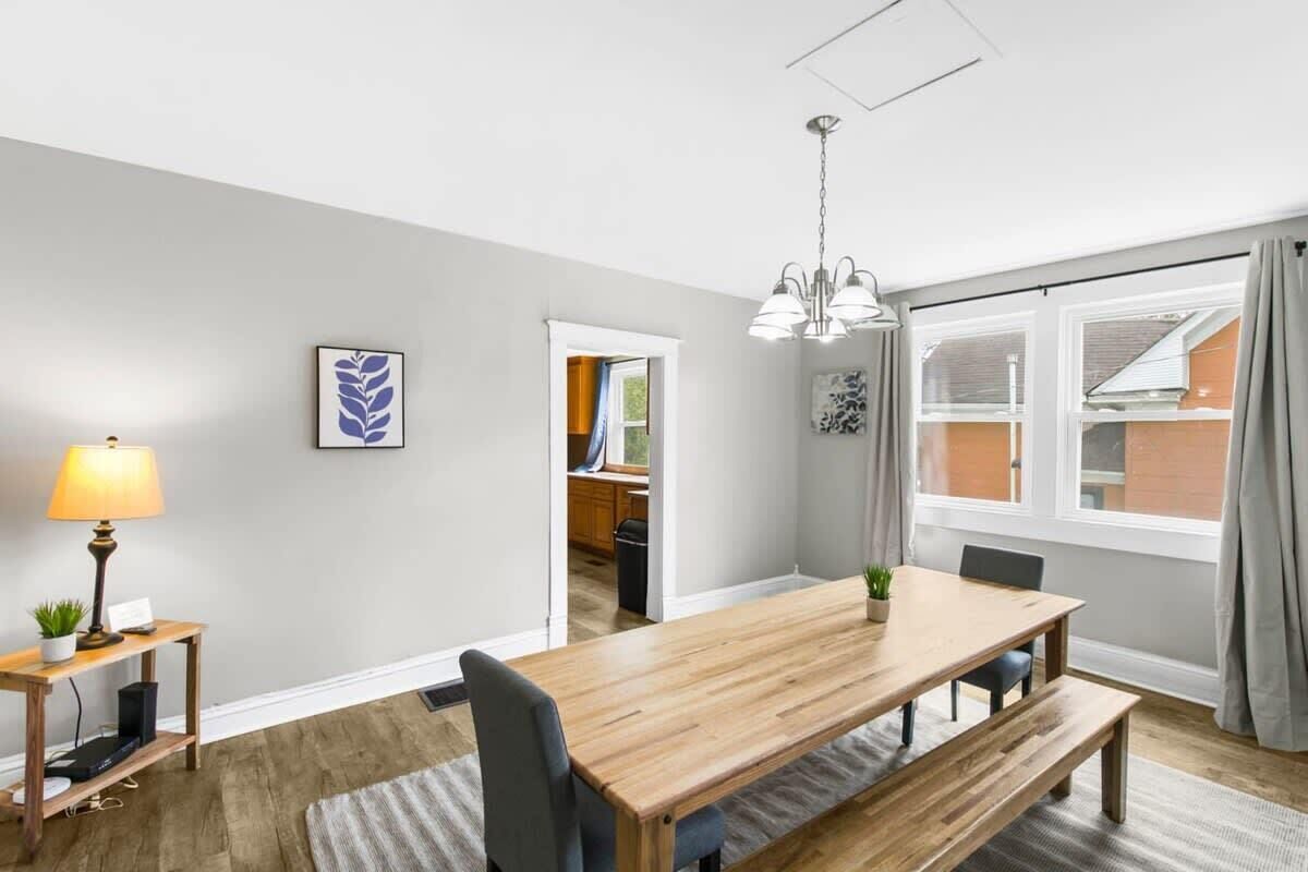 A dining area with a wooden table, chairs, a lamp, and a view of the outside.
