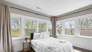 Una camera da letto con un letto grande, diverse finestre, un tavolino e una pianta.