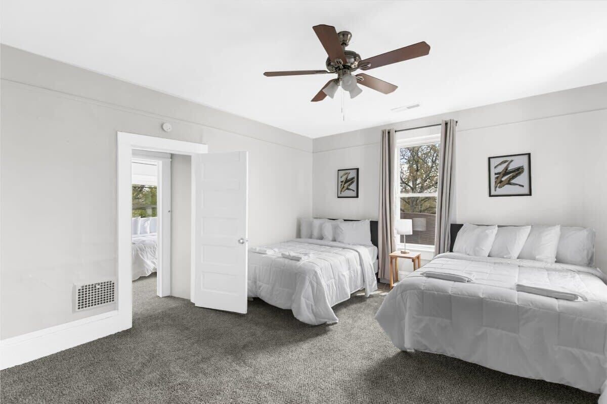 Un dormitorio con dos camas, un ventilador de techo y una puerta que da a otra habitación.