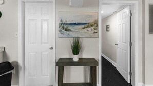 A hallway with a white door, a painting of a beach, and a small table with a plant. - Dugan Ave Unit B (Birmingham)