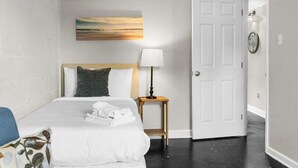 A hotel room with a bed, a bedside lamp, a painting on the wall, and a door. - Dugan Ave Unit B (Birmingham)