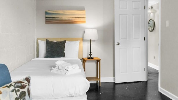 A hotel room with a bed, a bedside lamp, a painting on the wall, and a door. - Dugan Ave Unit B (Birmingham)