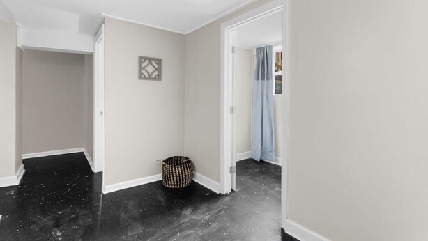 A hallway with a black floor, white walls, and a door leading to another room. - Dugan Ave Unit B (Birmingham)