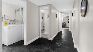 A hallway with a laundry area on the left, a door leading to another room, and a wall-mounted clock. - Dugan Ave Unit B (Birmingham)