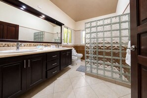 Une salle de bain avec un grand miroir, des meubles sombres, un lavabo, des toilettes et une douche en verre.