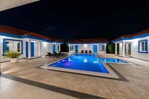 A swimming pool with lounge chairs, a potted plant, and a building with blue trim and red-tiled roofs.