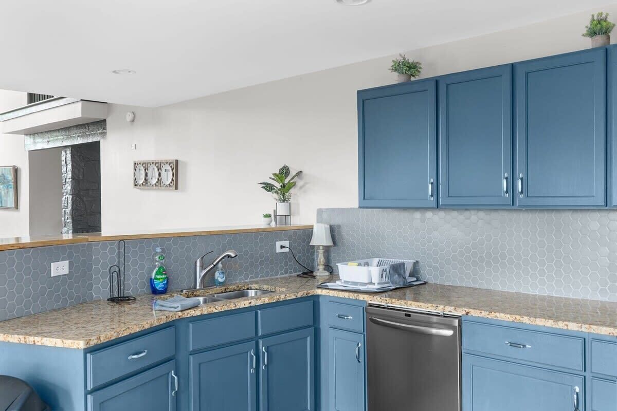 A modern kitchen with blue cabinets, a granite countertop, and a dishwasher.