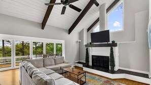 A modern living room with a sectional sofa, a fireplace, a television, and large windows overlooking a deck. - Observatory Drive Terrace House (Birmingham)
