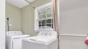 A laundry room with two white washing machines and a window with a curtain. - Bethany B Huntsville Oasis (Huntsville)