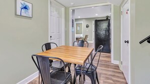 A dining area with a wooden table and black chairs, a framed picture on the wall, and a view into another room with a dark door. - Bethany B Huntsville Oasis (Huntsville)