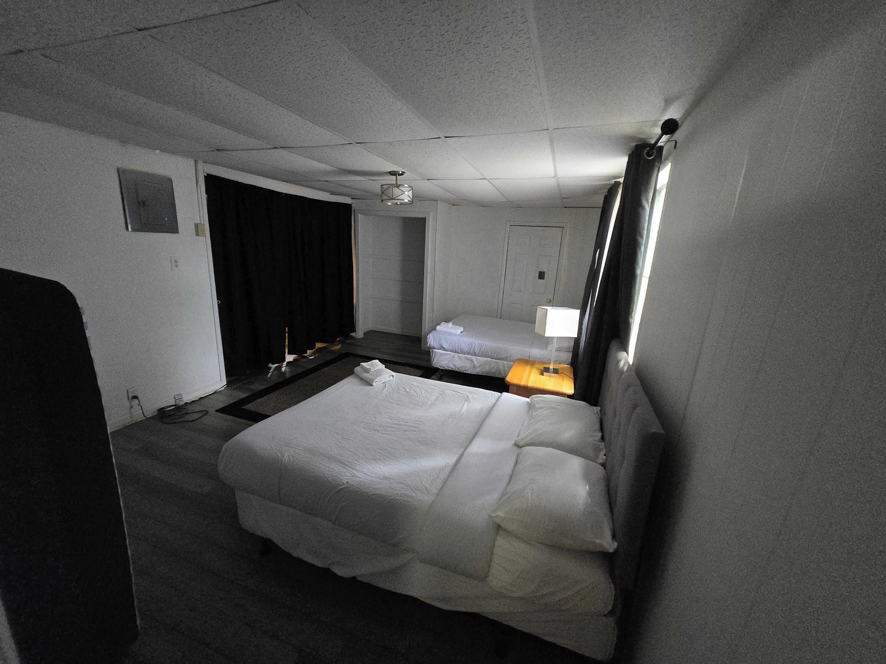 Een hotelkamer met een groot bed, een kleiner bed, een bureau met een lamp, een plafondventilator en een raam met gordijnen.