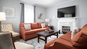 A living room with a sofa set, a coffee table, a fireplace, and a flat-screen TV mounted above it. - 4th St Little Blue in Bham (Birmingham)