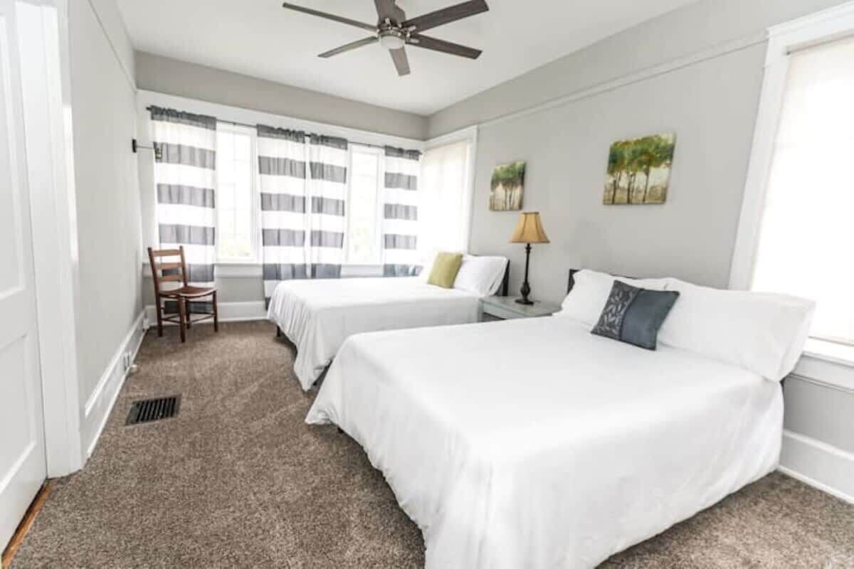 Habitación de hotel con dos camas, un ventilador de techo, una ventana con cortinas a rayas y una silla.