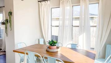A dining area with a wooden table and light blue chairs, a chandelier, and white curtains.