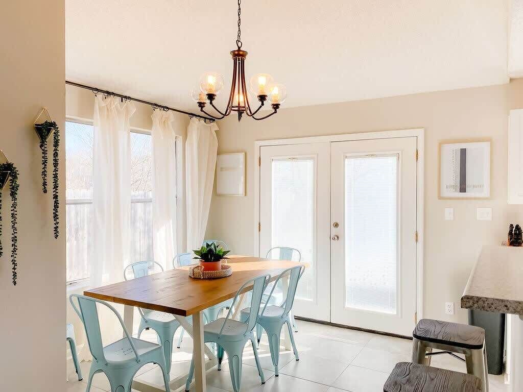A dining area with a wooden table, light blue chairs, a chandelier, and a sliding glass door.