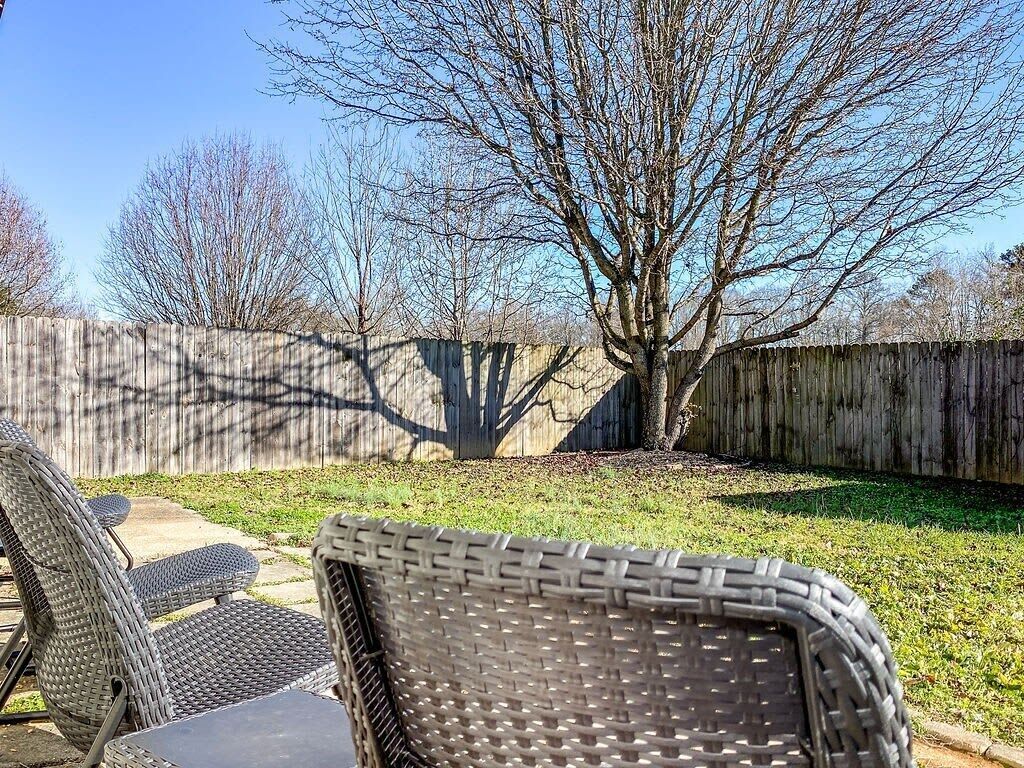 A backyard with a wooden fence, a tree, and wicker furniture.