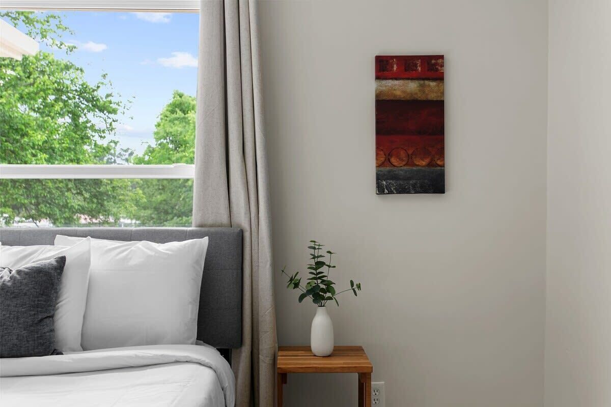 A bedroom with a bed, a bedside table with a plant, and a painting on the wall.