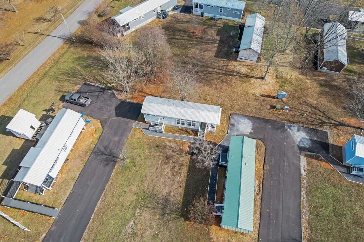 An aerial view of a residential area with multiple houses, a central building with a green roof, and a paved driveway.