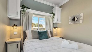 A neatly arranged bedroom with a large bed, two bedside tables, and a window with curtains. - Byrd 7 Nesting Nook (Owens Cross Roads)