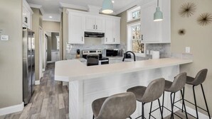 A modern kitchen with white cabinets, a large island with bar stools, and pendant lighting. - Byrd 7 Nesting Nook (Owens Cross Roads)