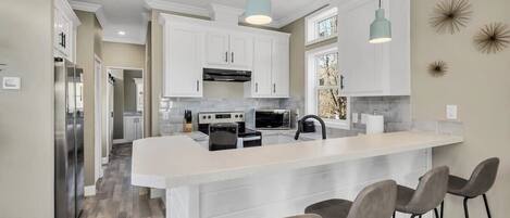 A modern kitchen with white cabinets, a large island with bar stools, and pendant lighting.